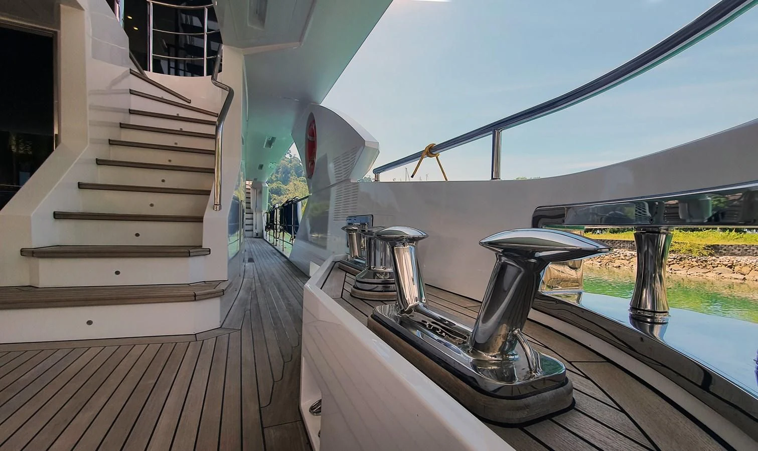 a deck with a large grill and a railing with a view of a lake and trees aboard CALYPSO Yacht for Charter