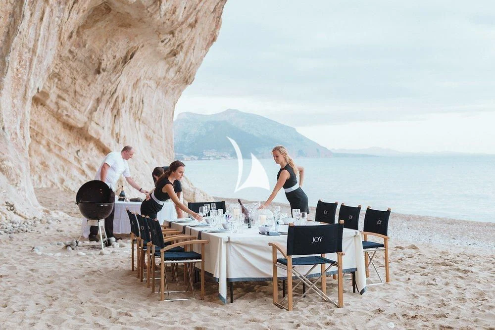 a group of people sitting around a table on a beach aboard JOY Yacht for Sale