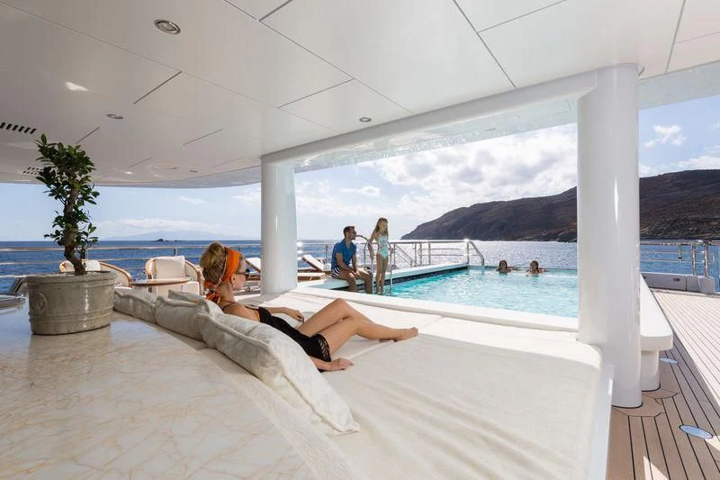 a person lying on a lounge chair on a deck by a pool aboard PLVS VLTRA Yacht for Sale