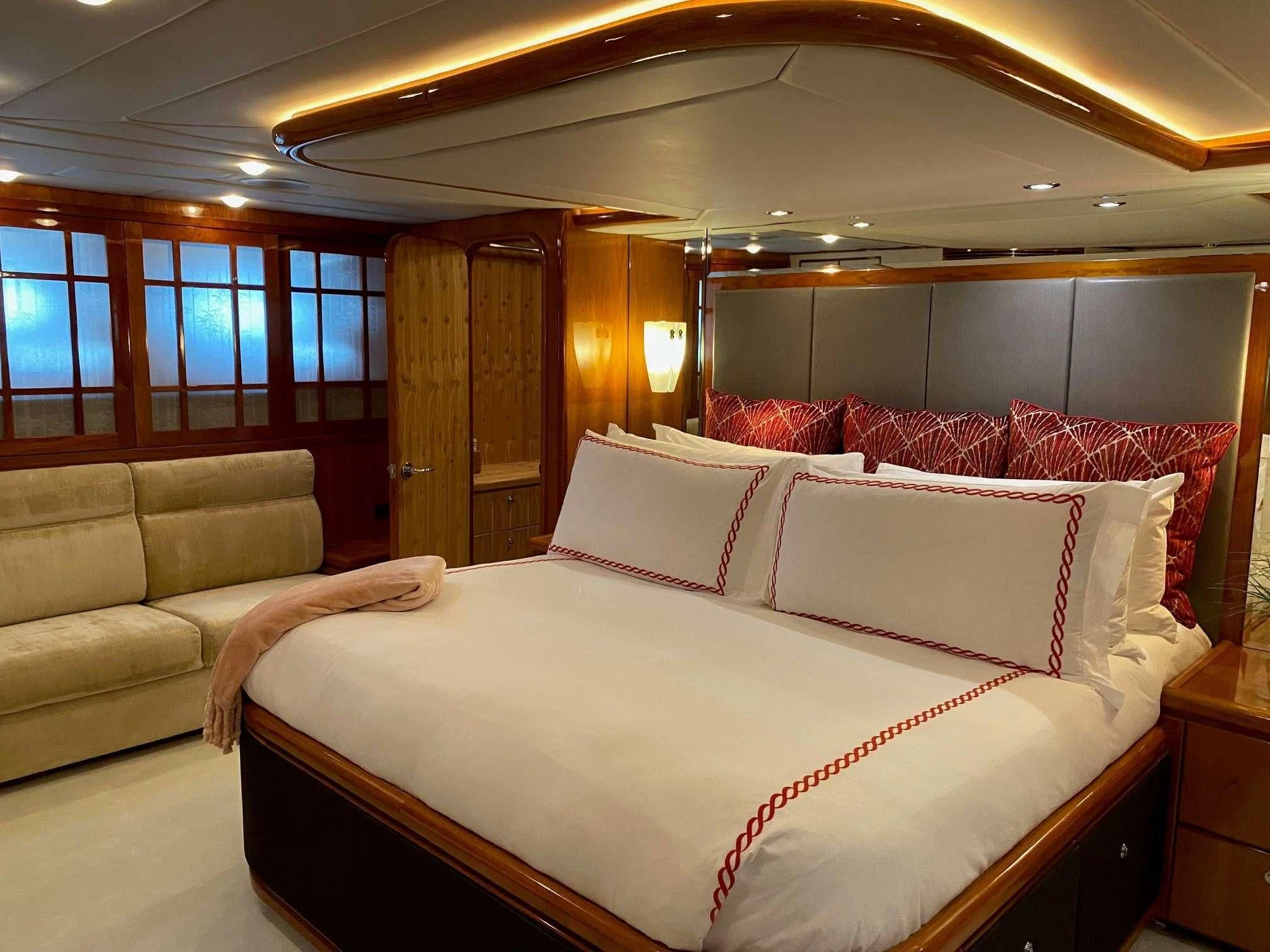 a bed with a white sheet and pillows in a room with a couch and a wood door aboard SLIPAWAY Yacht for Sale
