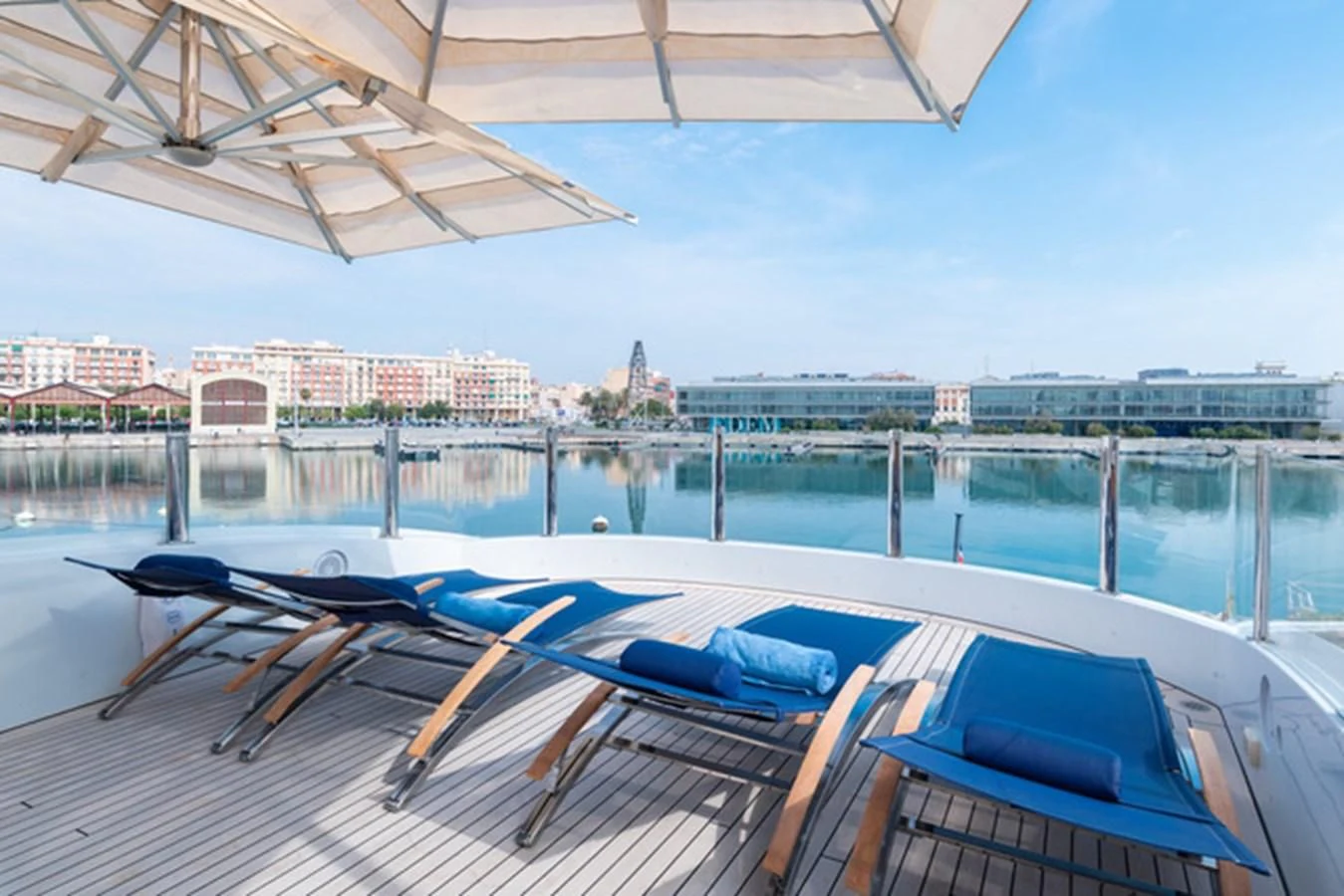 a pool with lounge chairs on the deck and a city in the background aboard ALI BABA Yacht for Sale