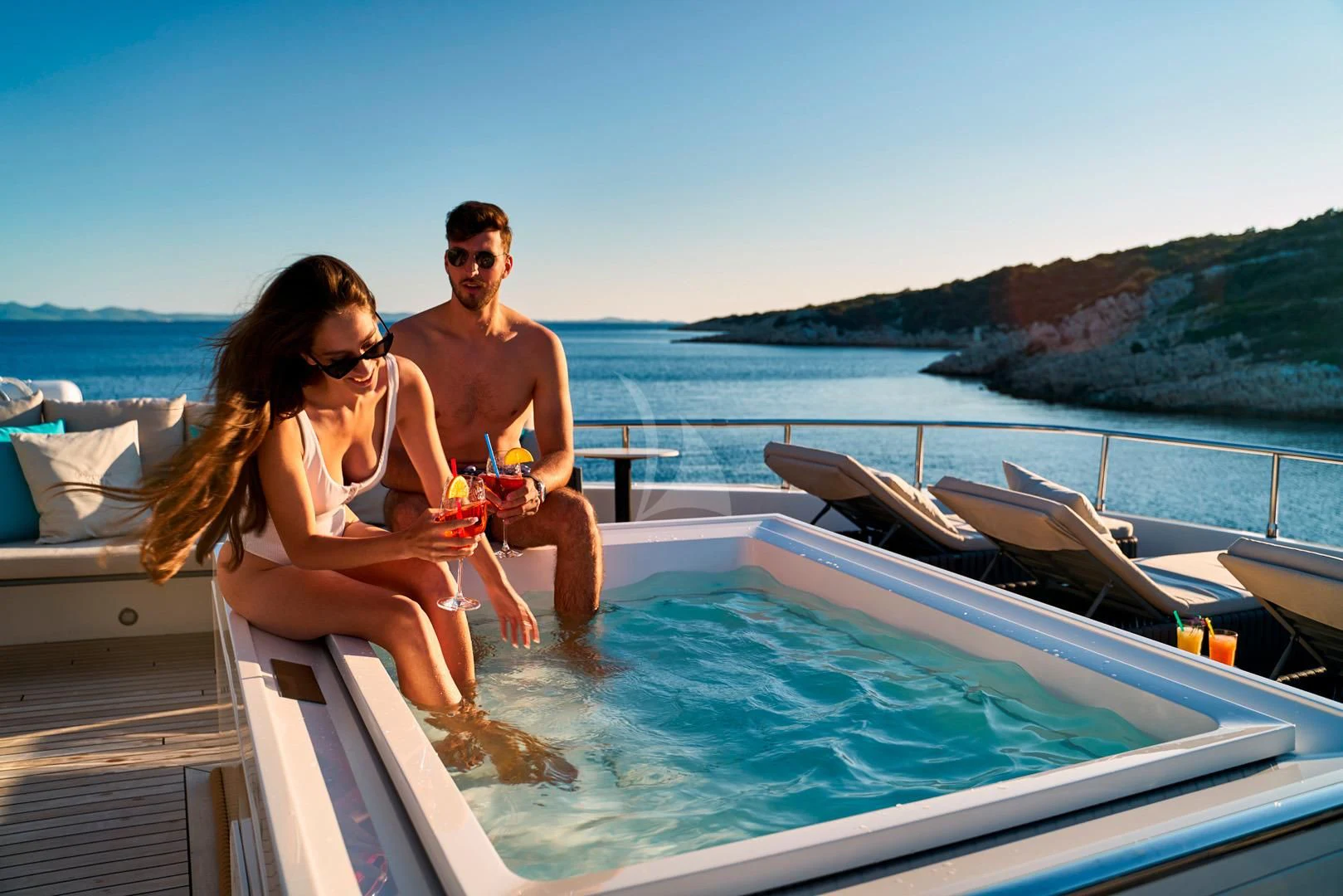 a man and woman sitting on a boat with a drink and a beach and water in the background aboard PRINCESS LONA Yacht for Sale