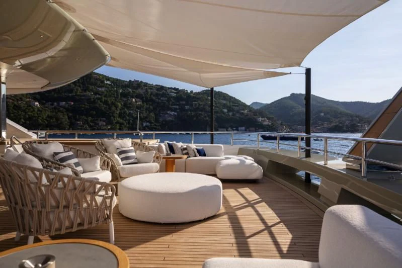 a large lounge area with a large body of water and mountains in the background aboard LADY A Yacht for Sale