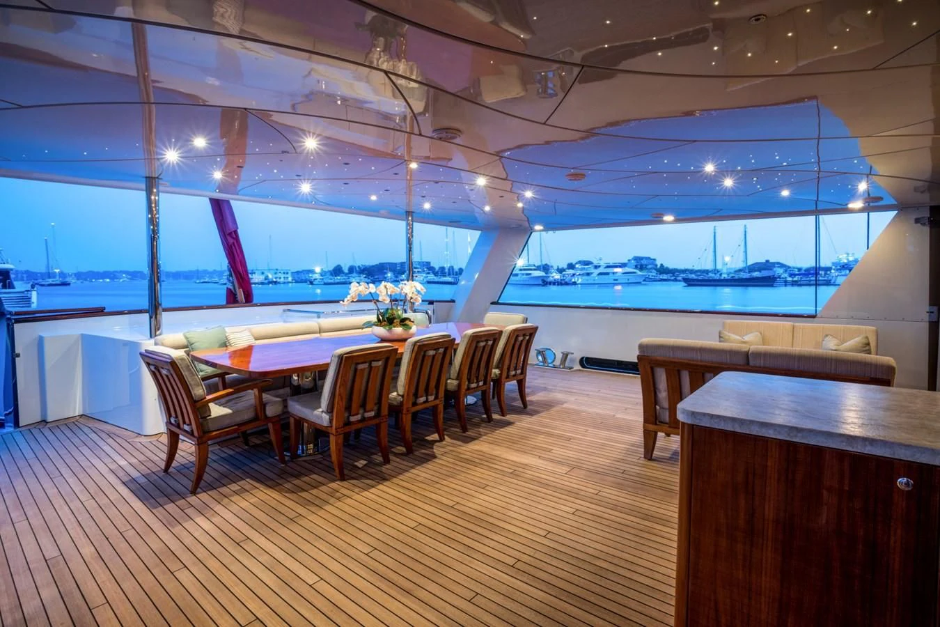 a room with a wood floor and a wood table with chairs and a large window with blue lights aboard HELIOS 2 Yacht for Sale