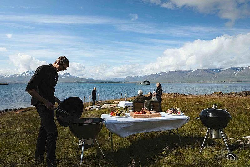 a person standing next to a table with a drum set and people on it aboard Q Yacht for Sale