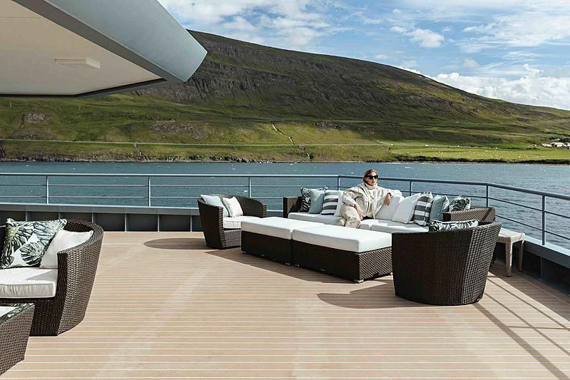 a person sitting on a couch on a deck overlooking a large body of water aboard Q Yacht for Sale