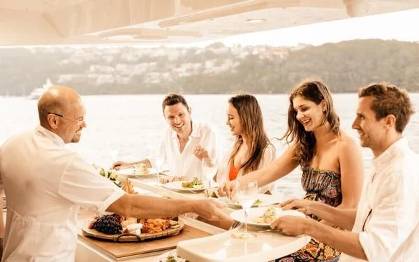 a group of people sitting at a table eating pizza aboard ONEWORLD Yacht for Sale