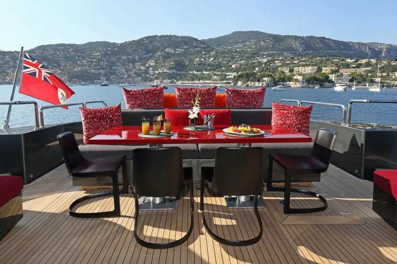 a table with chairs and a red tent on a deck with a body of water and mountains in aboard PRIMERO Yacht for Sale