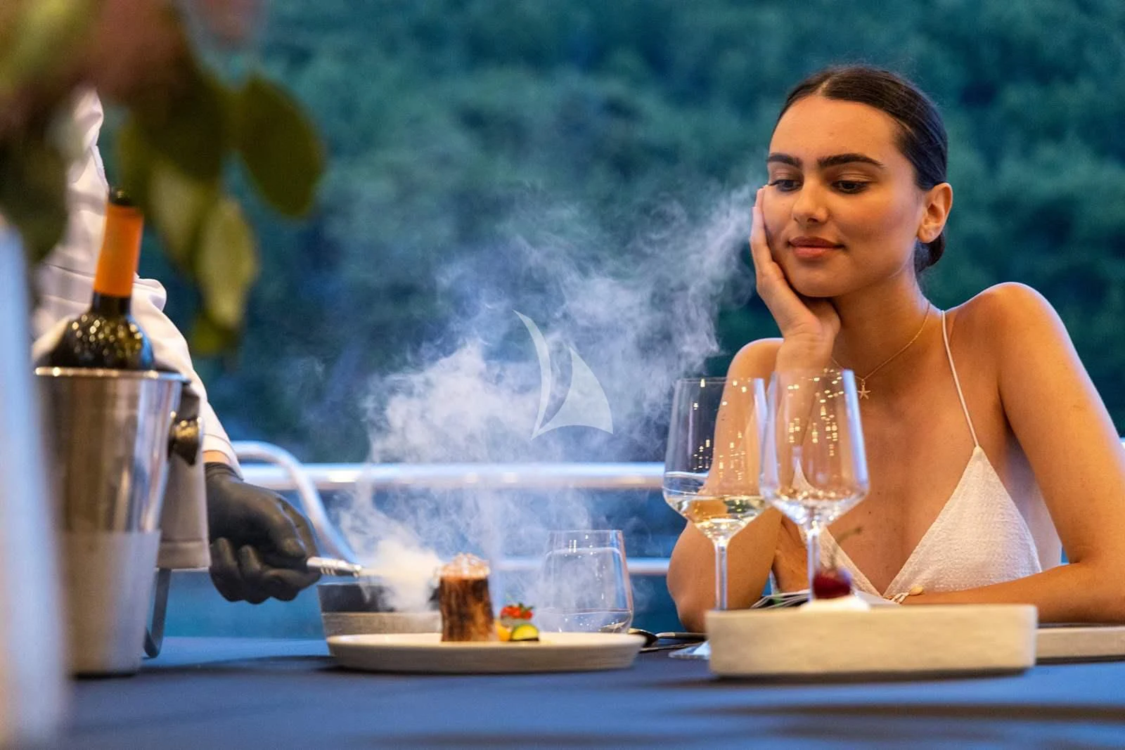 a person sitting at a table with a plate of food and a bottle of wine aboard NOCTURNO Yacht for Sale