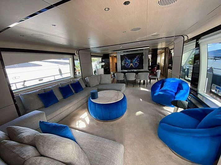 a large living room with a large blue couch and a large window aboard SOLSTICE Yacht for Sale