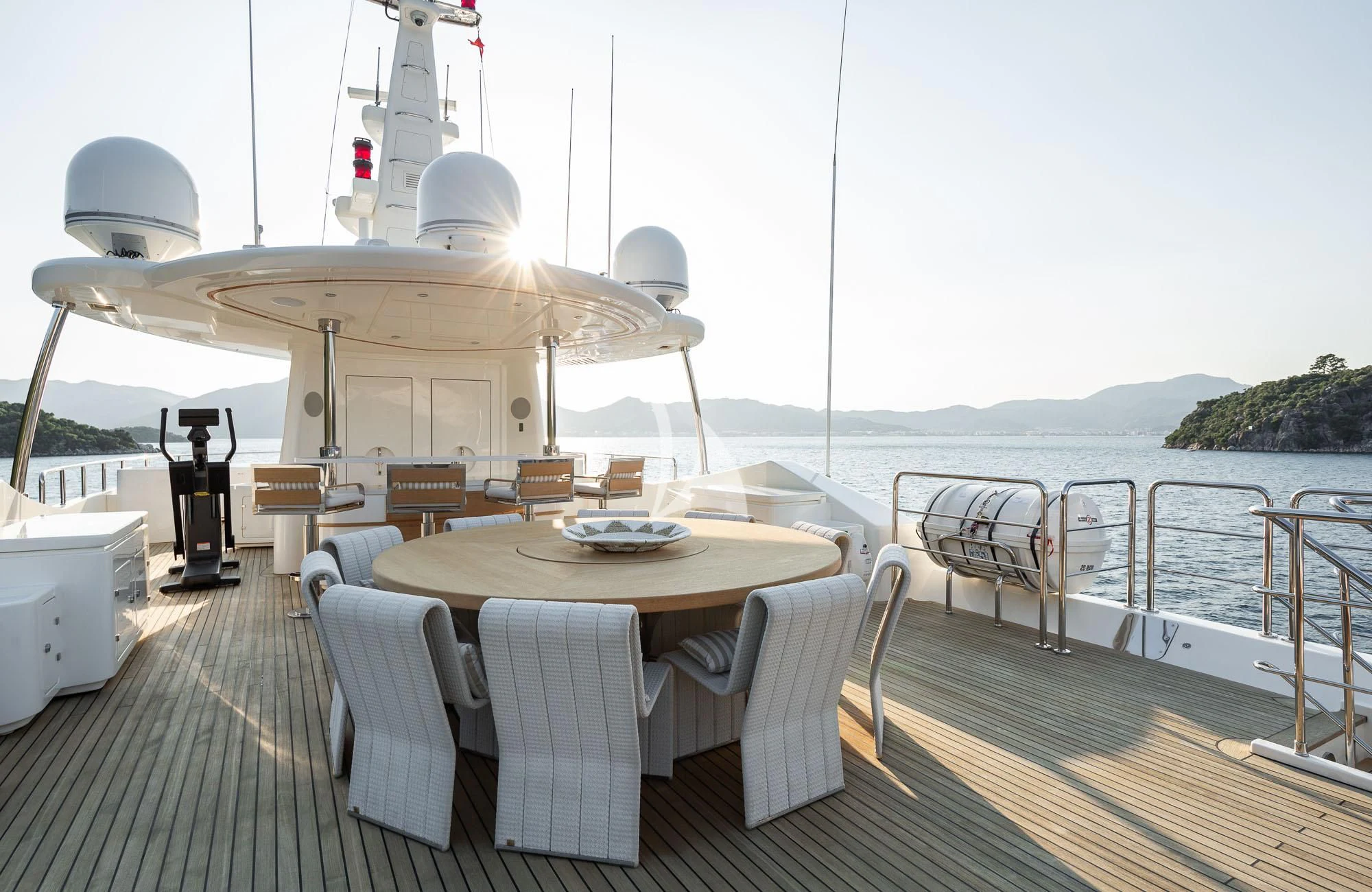 a table on a deck with chairs on it and a boat in the water in the background aboard LADY I Yacht for Charter