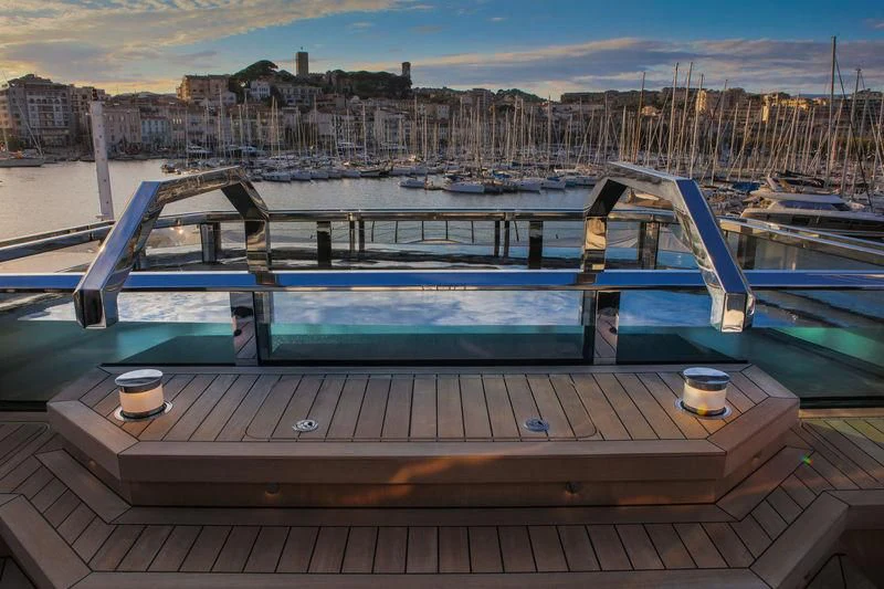 a deck with a drink and a cup on it by a body of water with boats in the aboard ATLANTE Yacht for Sale