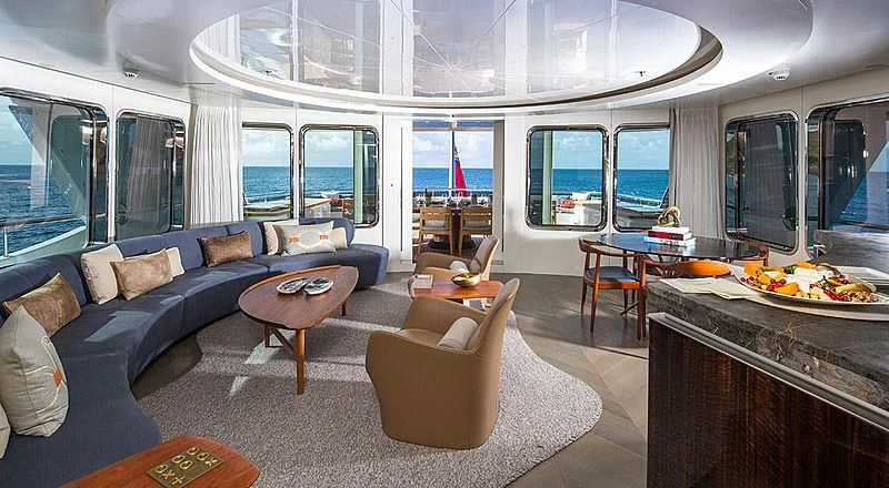 a living room with a blue couch and a large window aboard REVERIE Yacht for Sale