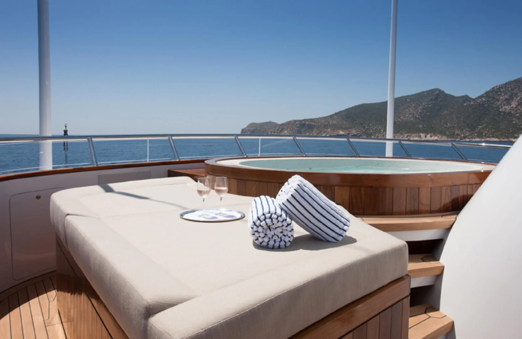 a table with a glass of wine on a balcony overlooking a body of water aboard MIRAGE Yacht for Sale