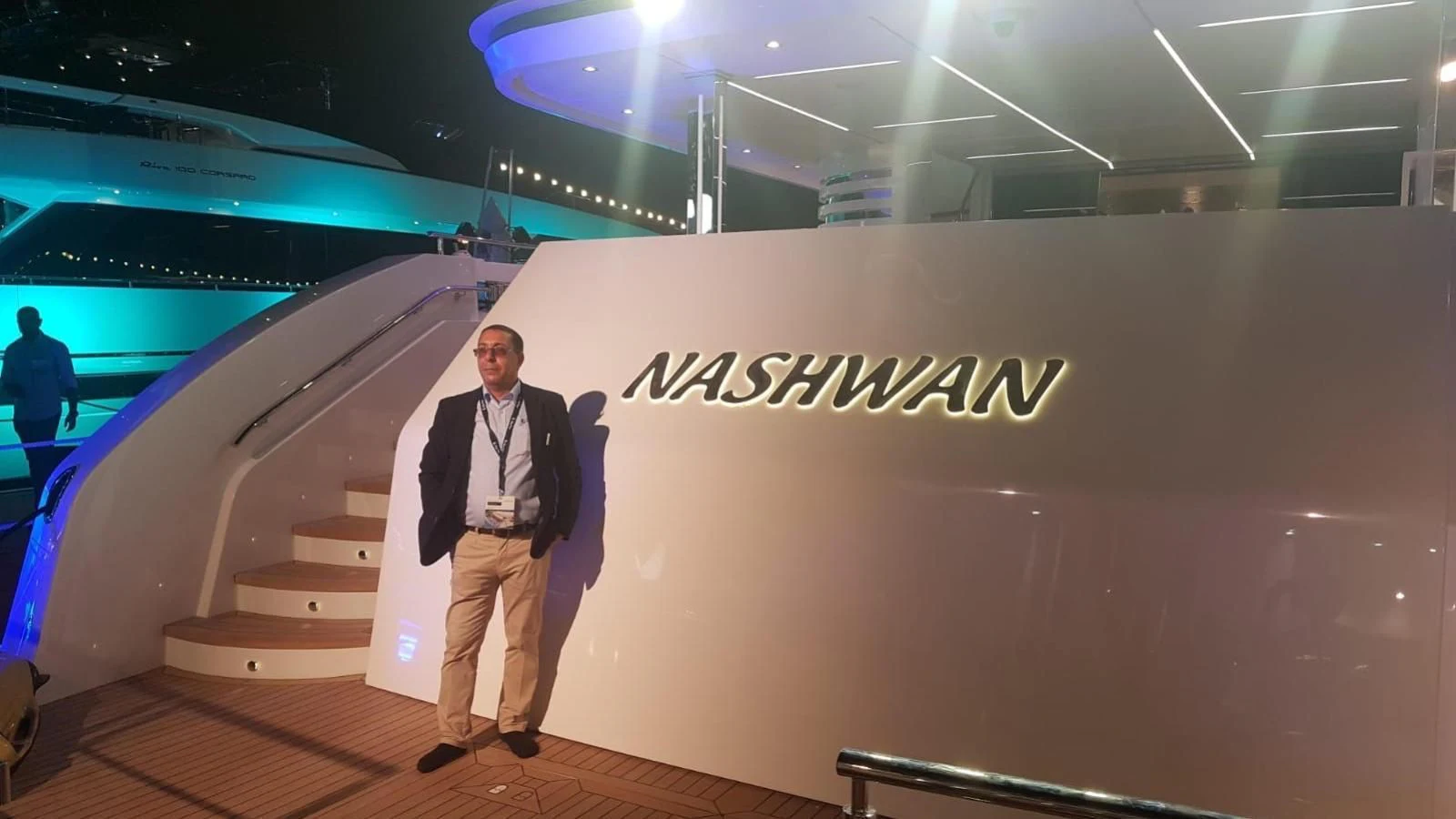 a person in a suit standing on a stage with a sign on the wall aboard NASHWAN Yacht for Sale