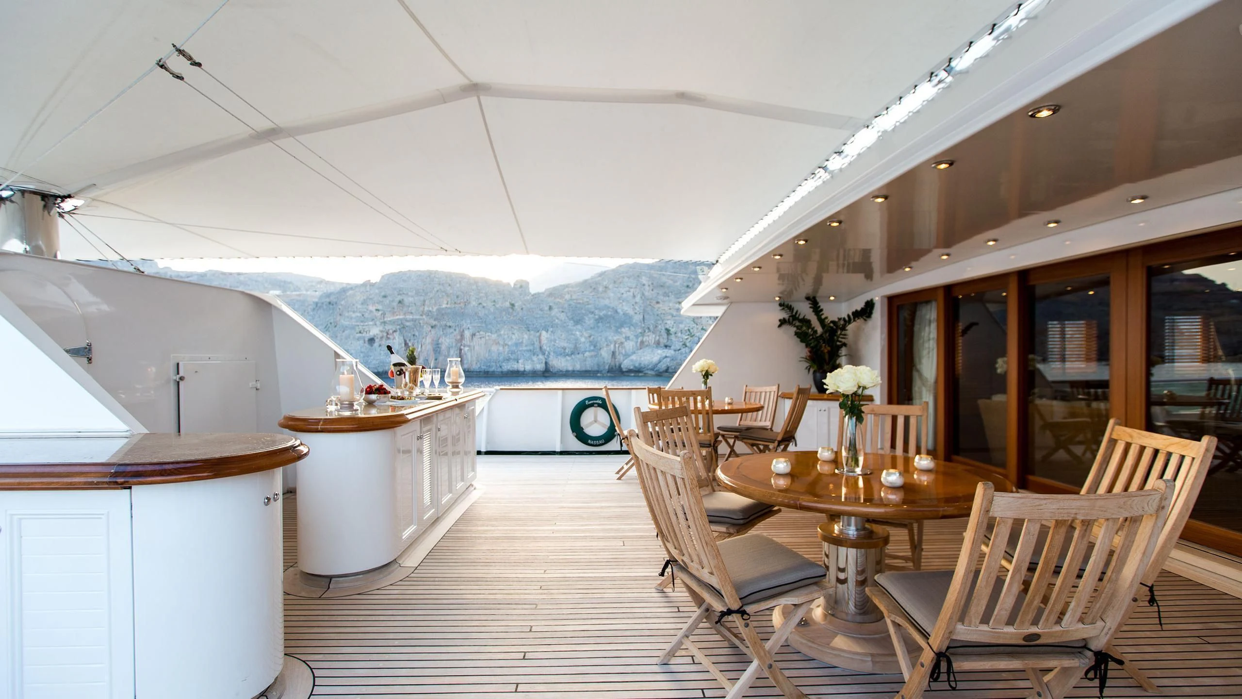 a wooden table and chairs on a deck with a view of the mountains aboard ESMERALDA Yacht for Sale