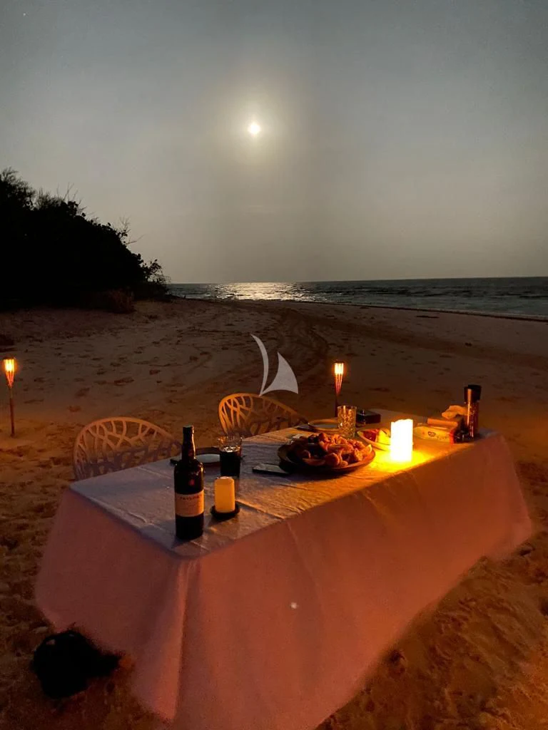 a table with food and bottles on it by a beach with a moon aboard GALAKTIKA SKAY Yacht for Sale