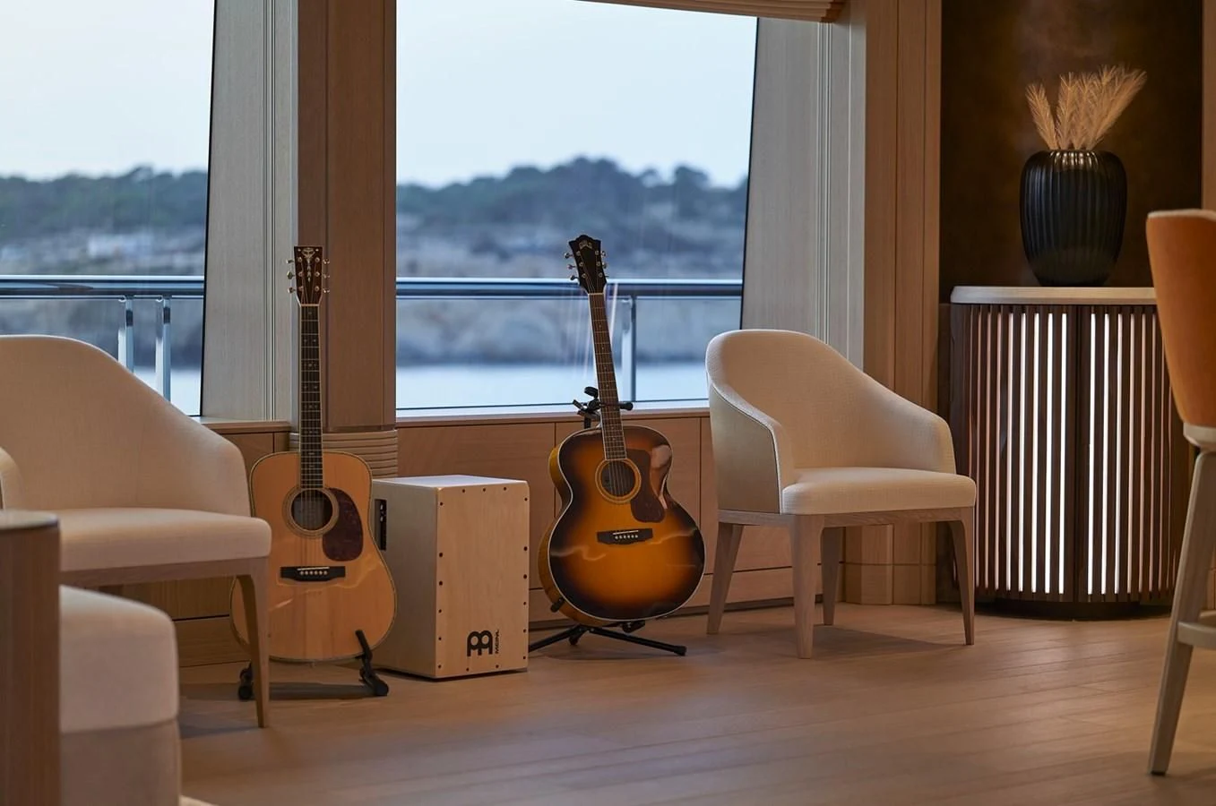 a guitar on a stand in a room with chairs and a window aboard COME TOGETHER Yacht for Charter