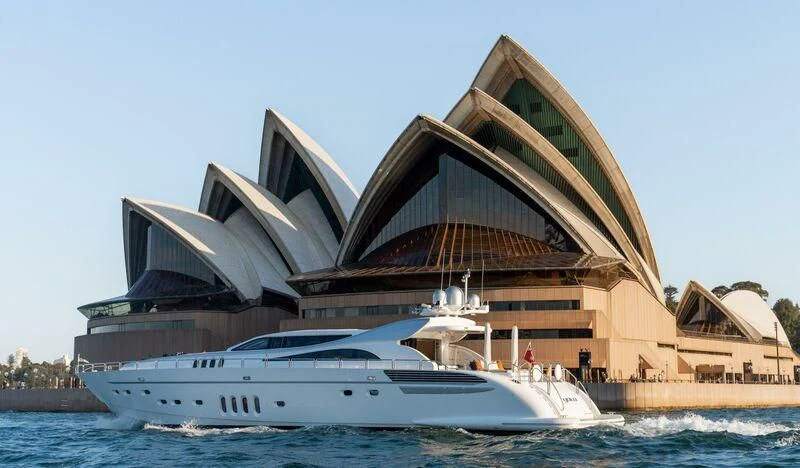 a large building with a dome with Sydney Opera House in the background aboard YOLO Yacht for Sale
