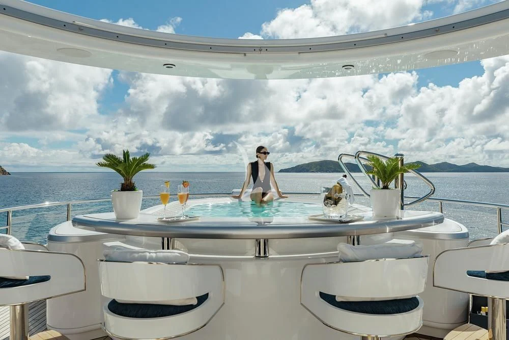 a person sitting at a table with a glass of wine and a view of the ocean aboard EXCELLENCE Yacht for Sale