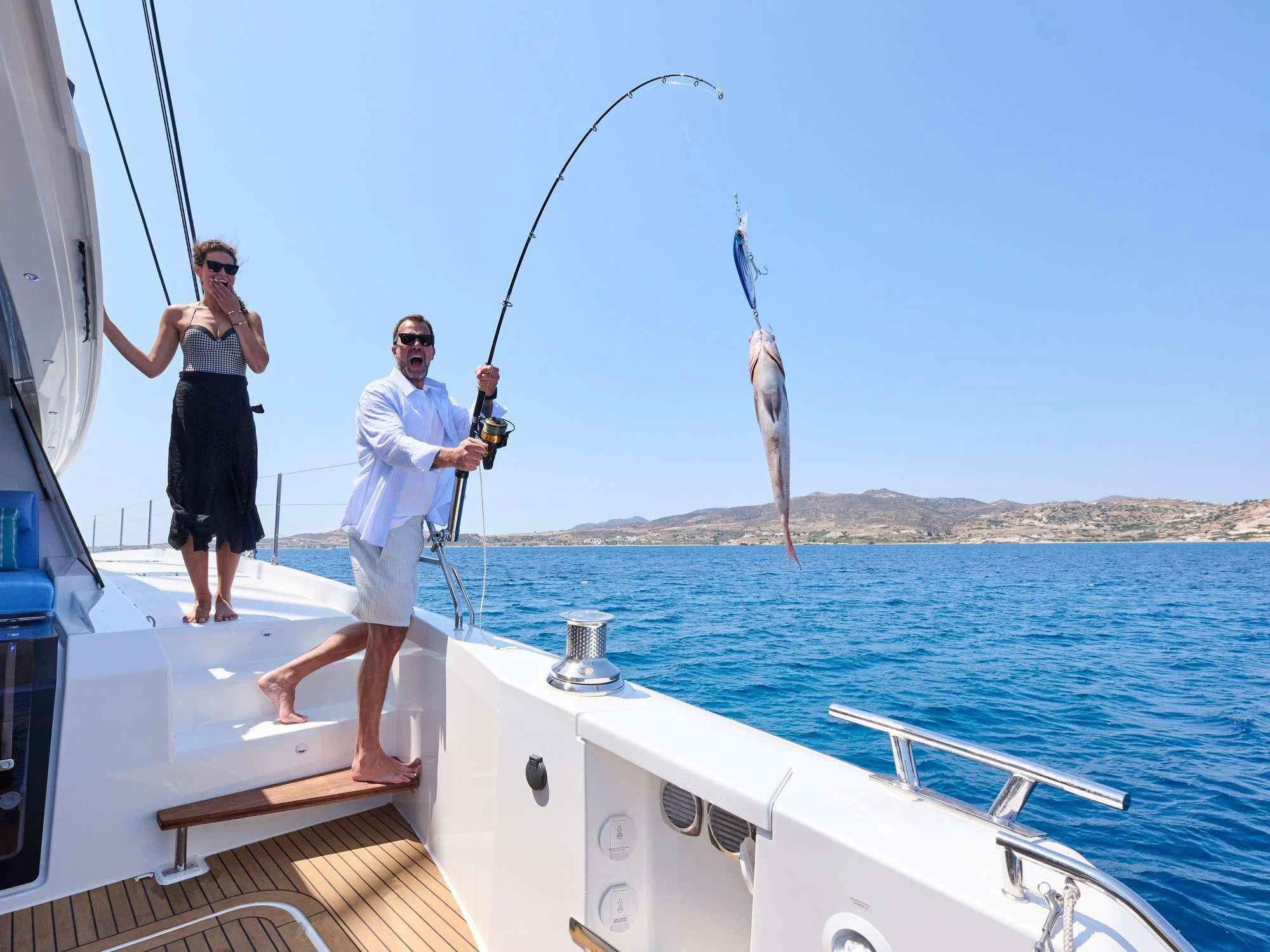 a man and woman standing on a boat holding a fishing pole aboard APHAEA Yacht for Charter