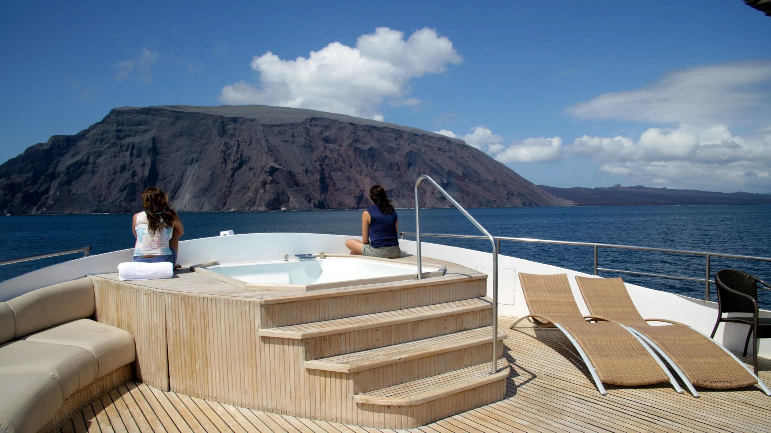 a couple of women sitting on a white table on a boat in the water with a mountain in aboard INTEGRITY Yacht for Sale