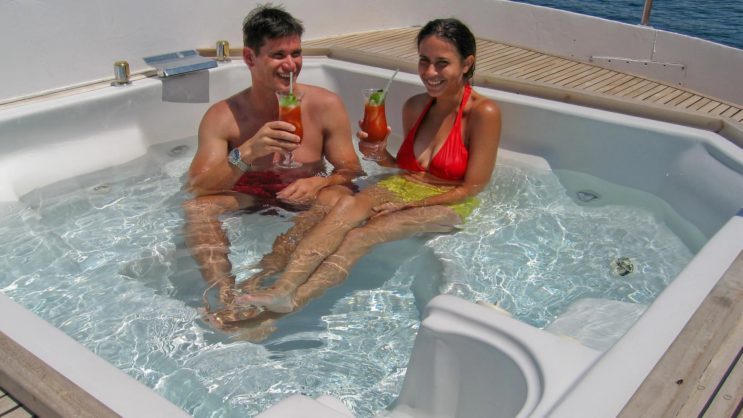 a man and woman sitting in a bathtub with drinks and a towel aboard INTEGRITY Yacht for Sale