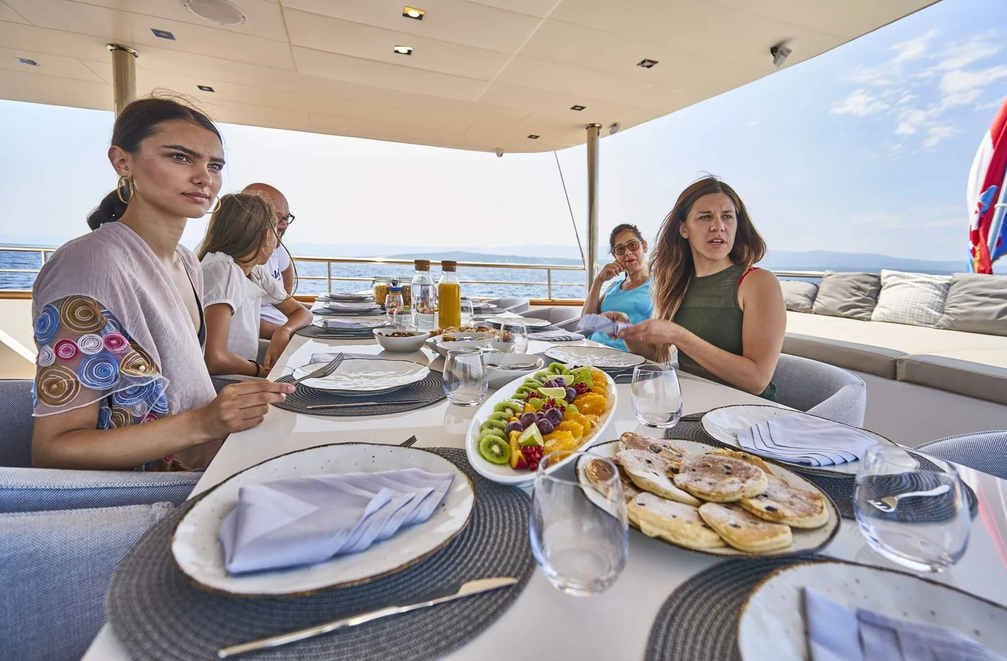 a group of people sitting at a table with food aboard DALMATINO Yacht for Sale