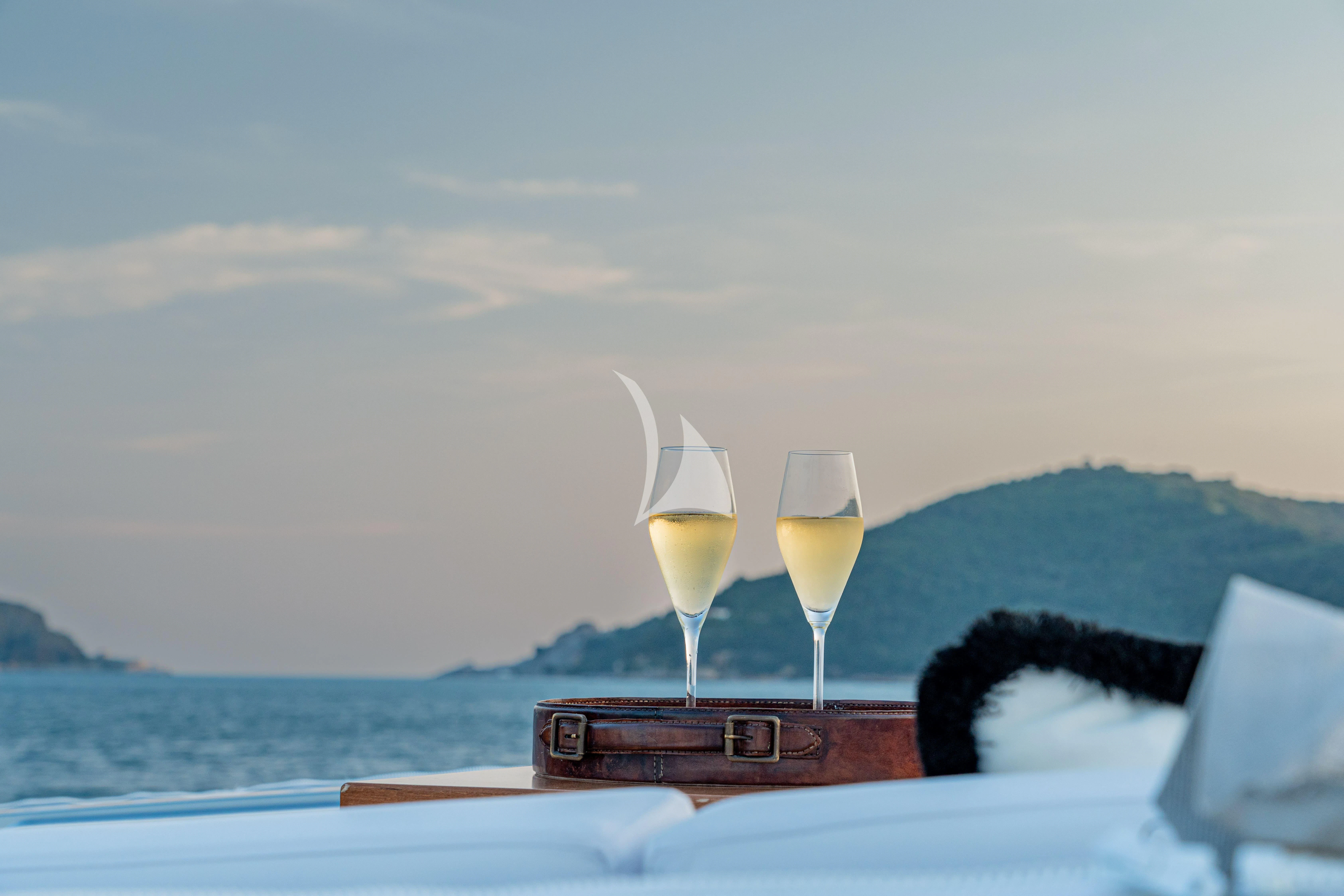 a couple of glasses of champagne on a table with a view of the ocean and mountains in the aboard MANU V Yacht for Sale