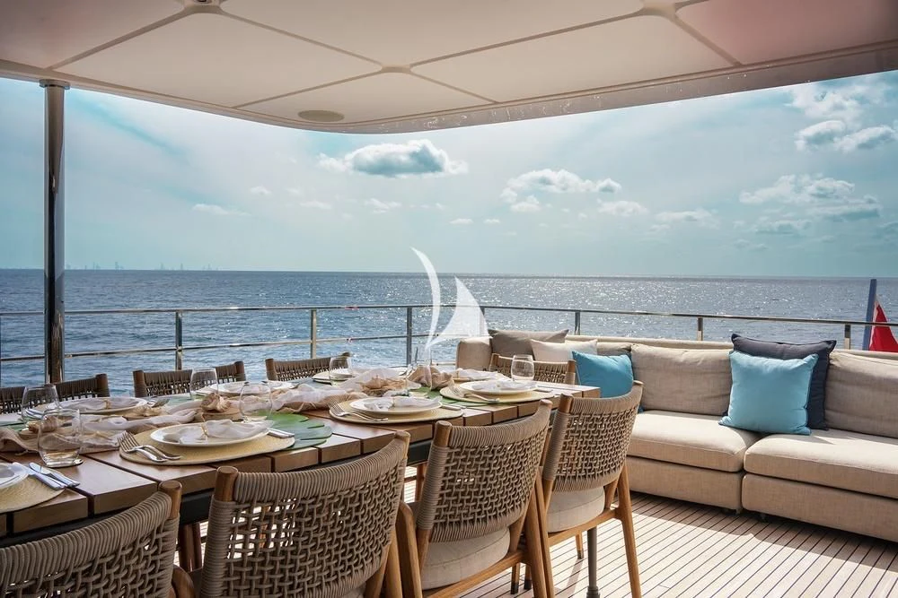 a table with chairs and a large body of water in the background aboard JYC Yacht for Sale