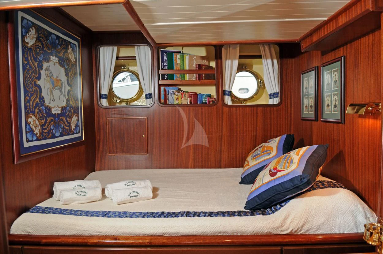 a bed with a blue and white sheet and a mirror above it aboard OFELIA Yacht for Sale