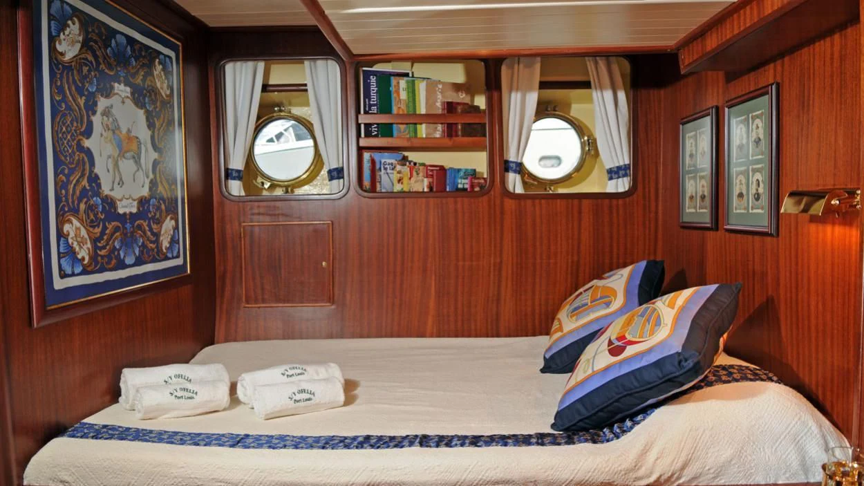 a bed with a blue and white bed spread and a mirror aboard OFELIA Yacht for Sale