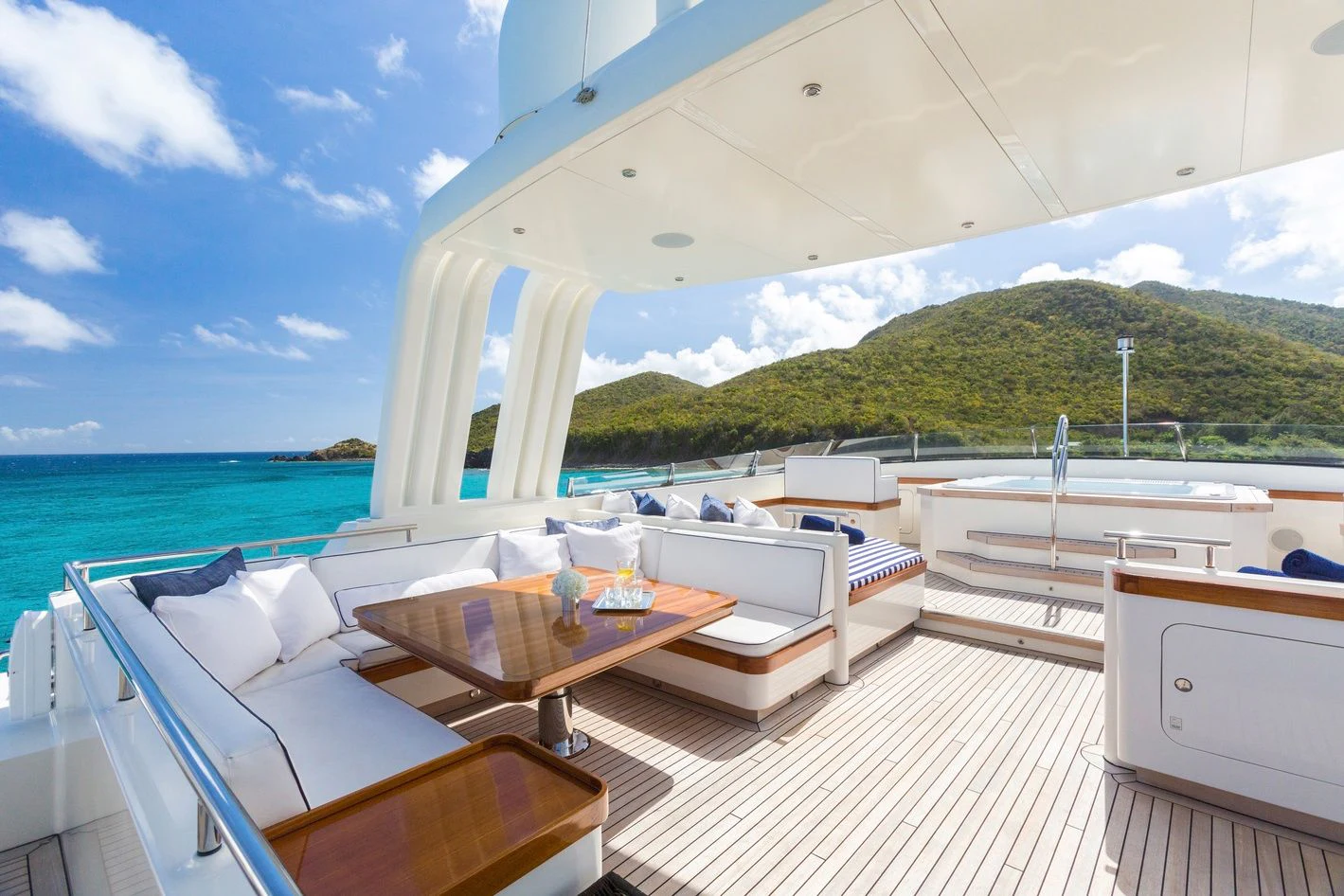a room with a table and chairs on a deck with a view of the ocean and a hill aboard FABULOUS CHARACTER Yacht for Charter