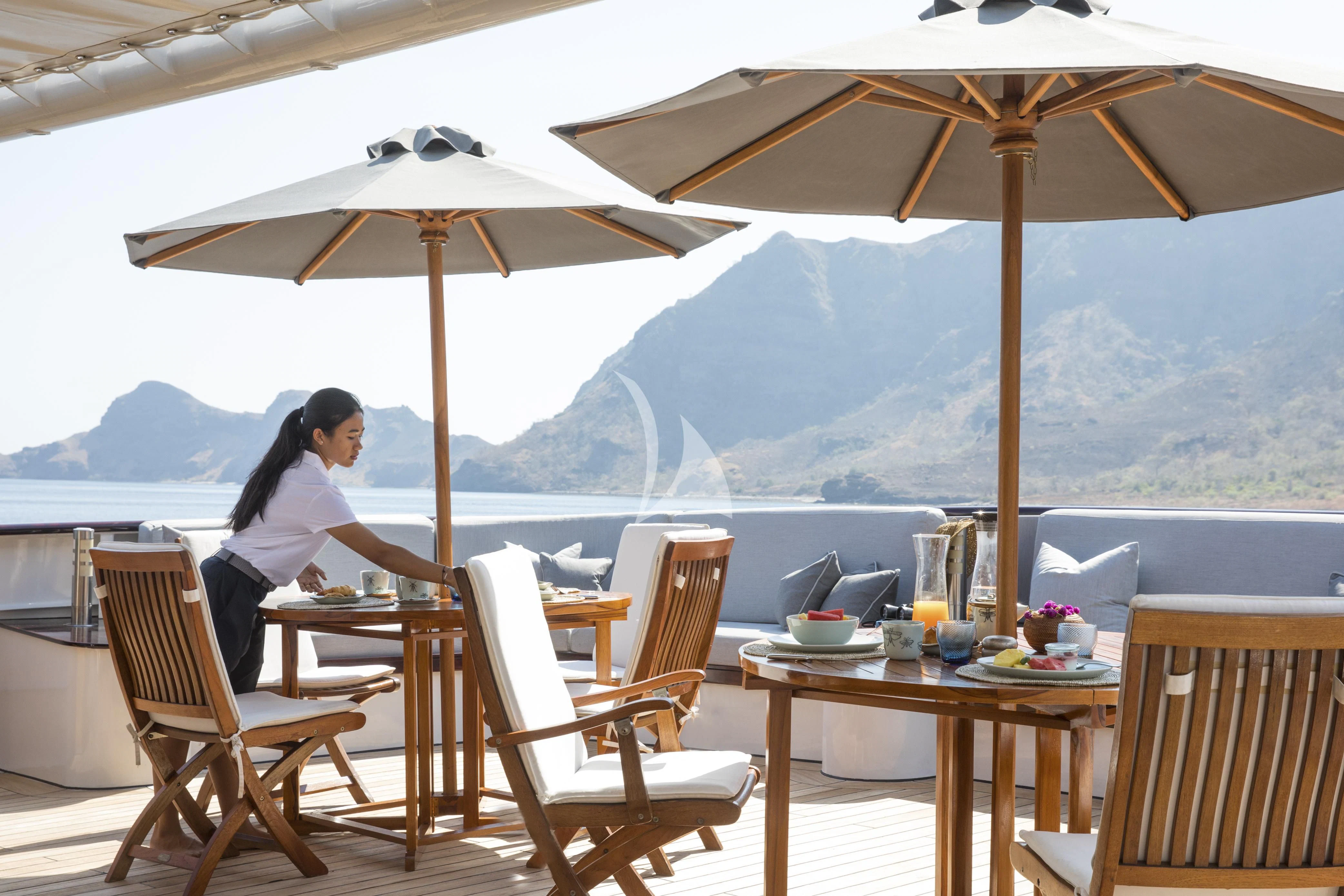 a person sitting at a table under an umbrella aboard AQUA BLU Yacht for Sale