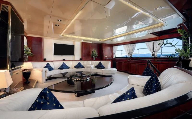 a large room with a large white bed and a table with blue pillows aboard LADY SUNSHINE Yacht for Sale