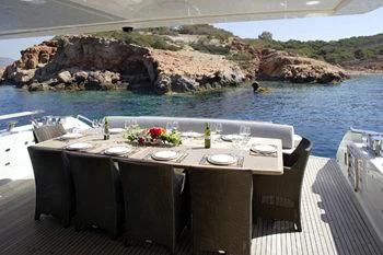 a table set for a meal on a balcony overlooking a body of water aboard DRAGON Yacht for Sale