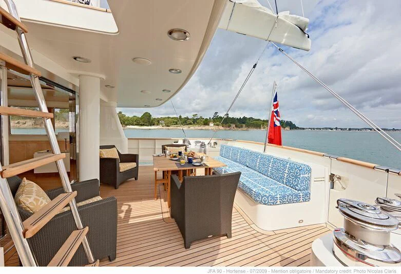 a deck with a pool and a deck with chairs and a table and chairs and a flag on aboard HORTENSE Yacht for Sale