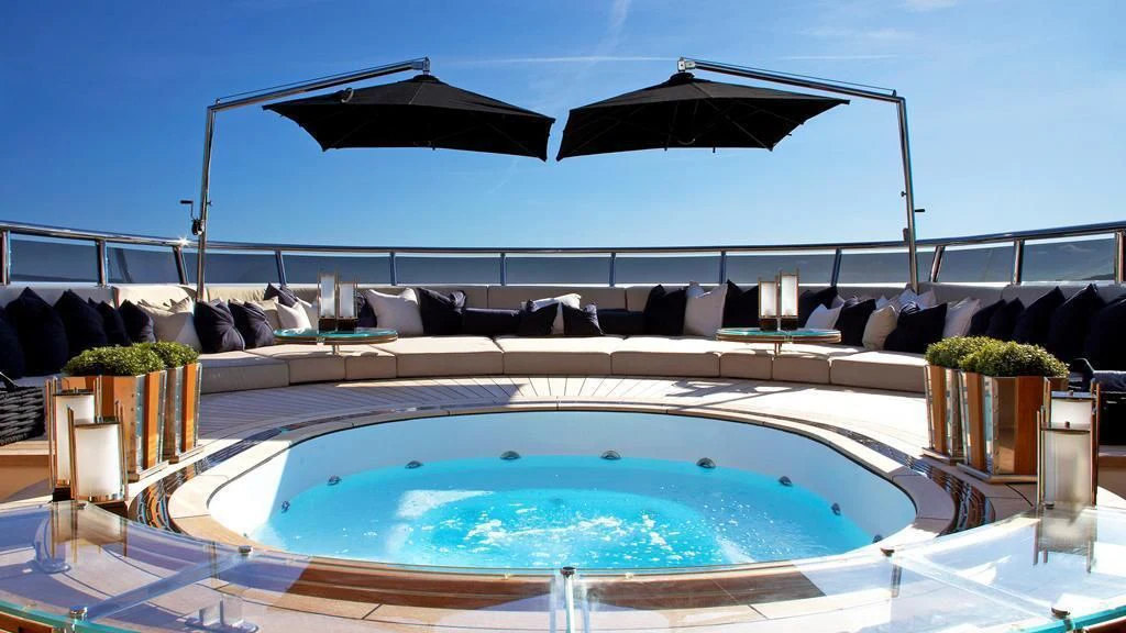 a swimming pool with a lounge chair and a large black umbrella on a sunny day aboard SEALION Yacht for Sale