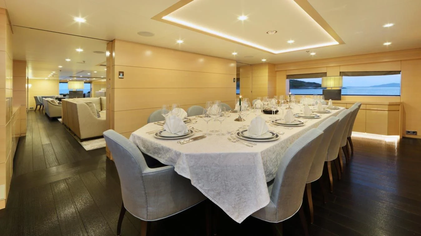 a large dining table with white cloths and chairs aboard EGO Yacht for Sale