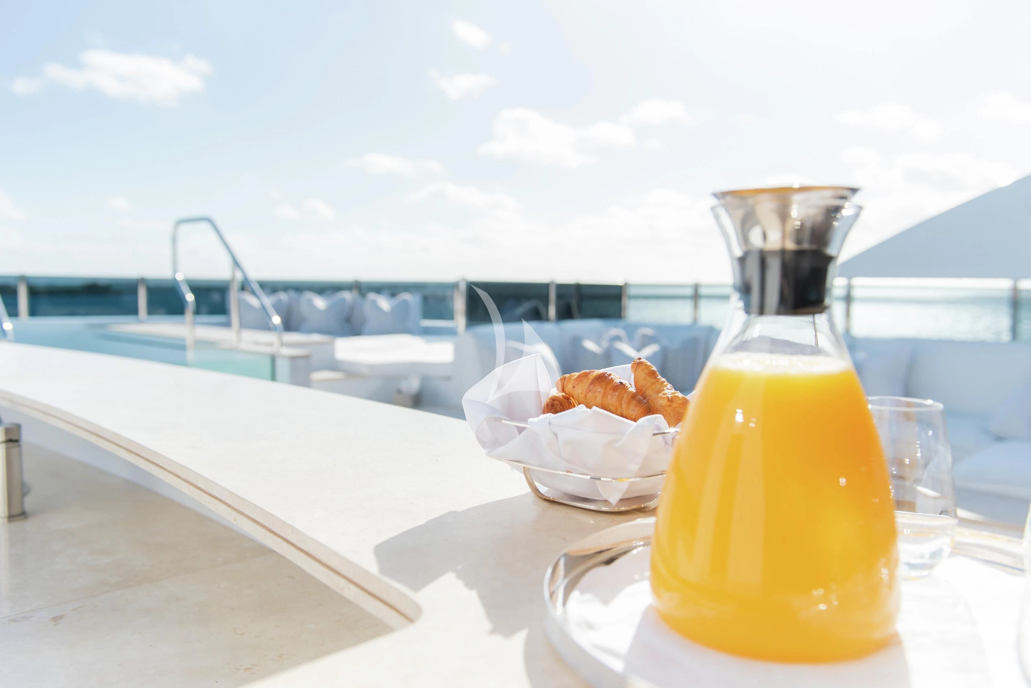 a glass bottle and a bowl of chicken on a table with a beach and water in the background aboard NORTH STAR Yacht for Sale