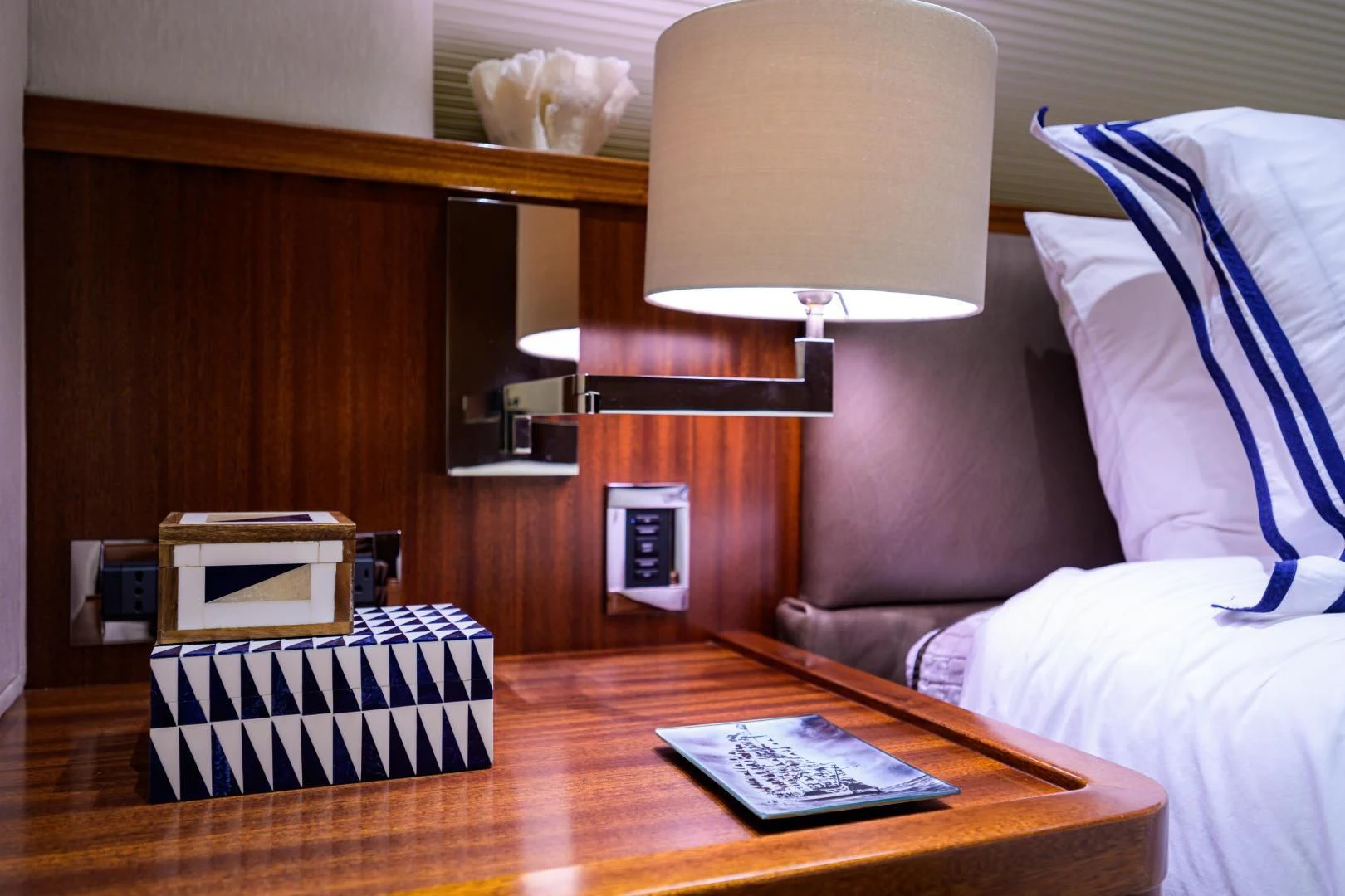 a bed with a pillow and a table with a book on it aboard LADY JJ Yacht for Charter