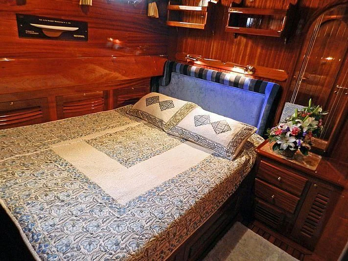 a bed with a white sheet and a blue pillow aboard AGANIPPE Yacht for Sale