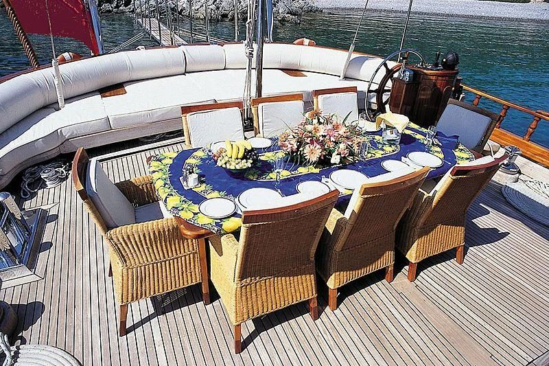 a table set with chairs and a boat on the water aboard AGANIPPE Yacht for Sale