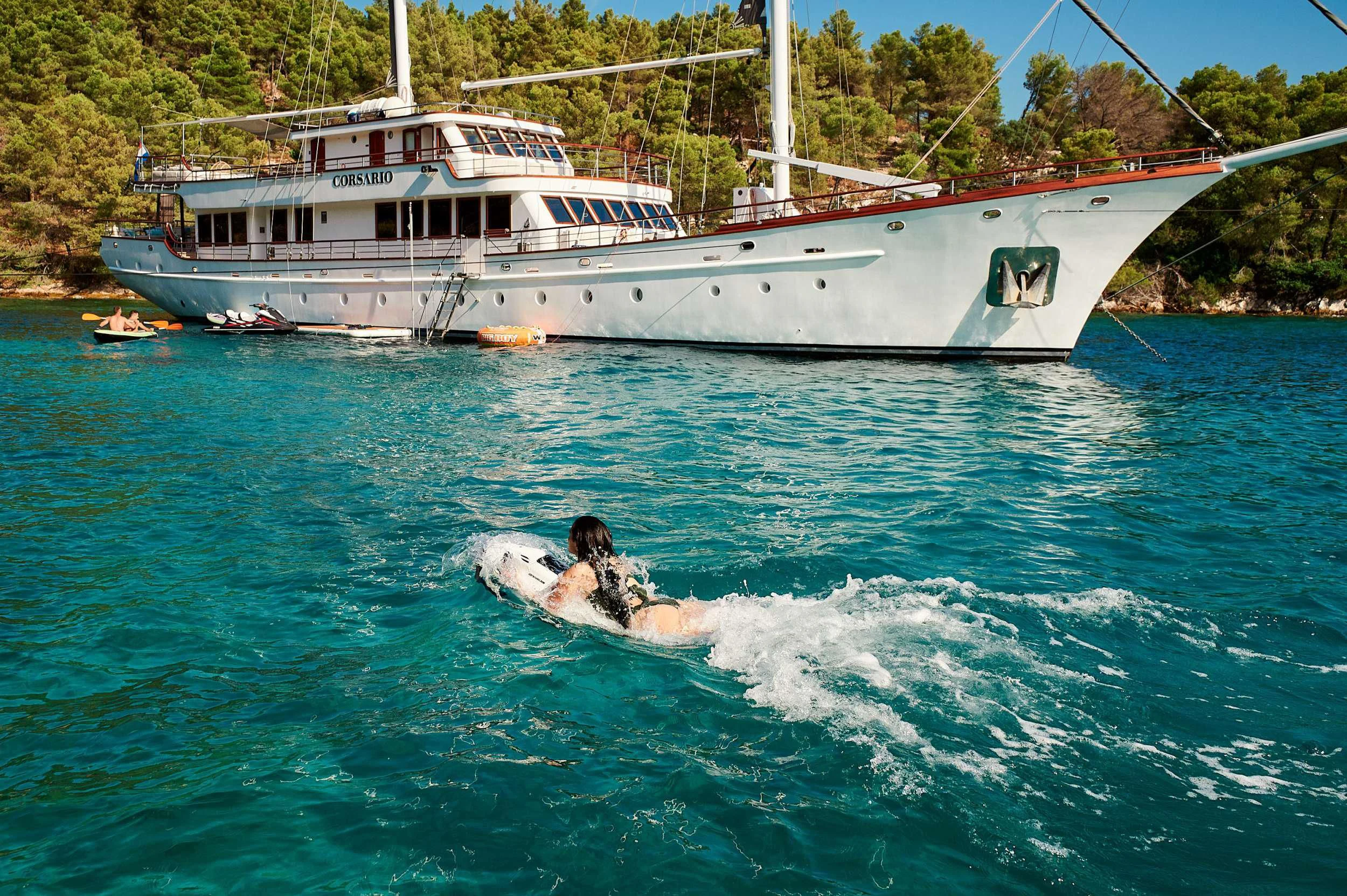 a person riding a surfboard in the water next to a boat aboard CORSARIO Yacht for Charter