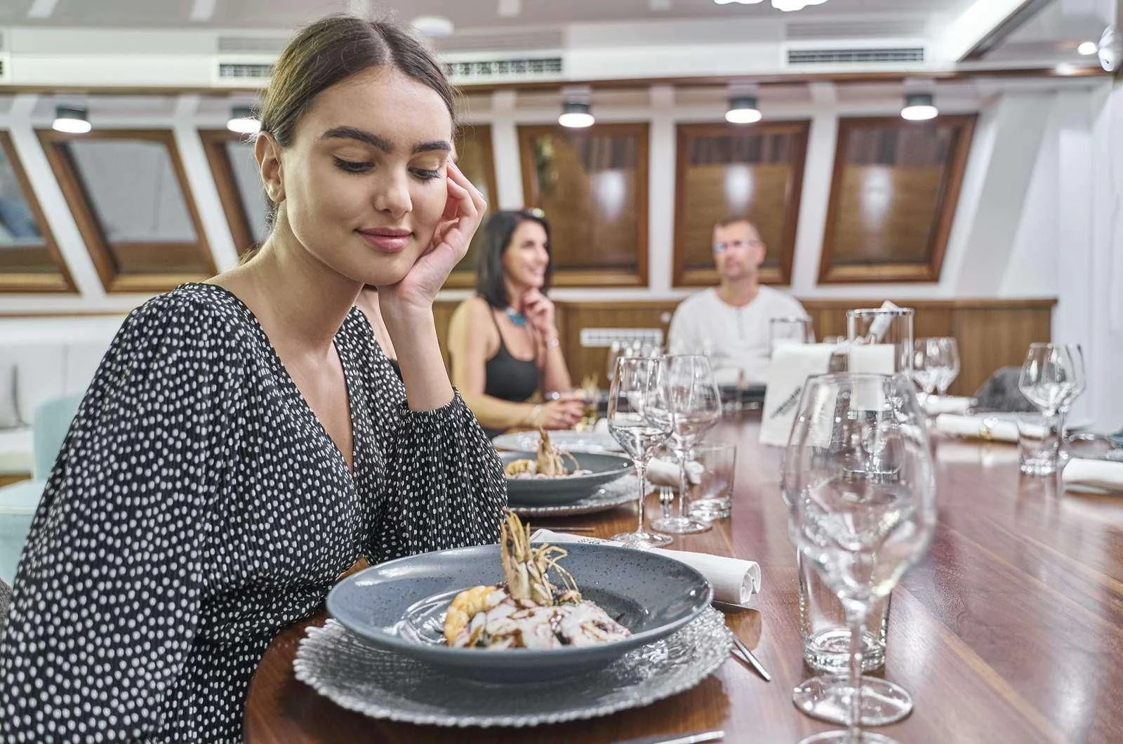 a woman sitting at a table with a plate of food and wine glasses aboard CORSARIO Yacht for Charter