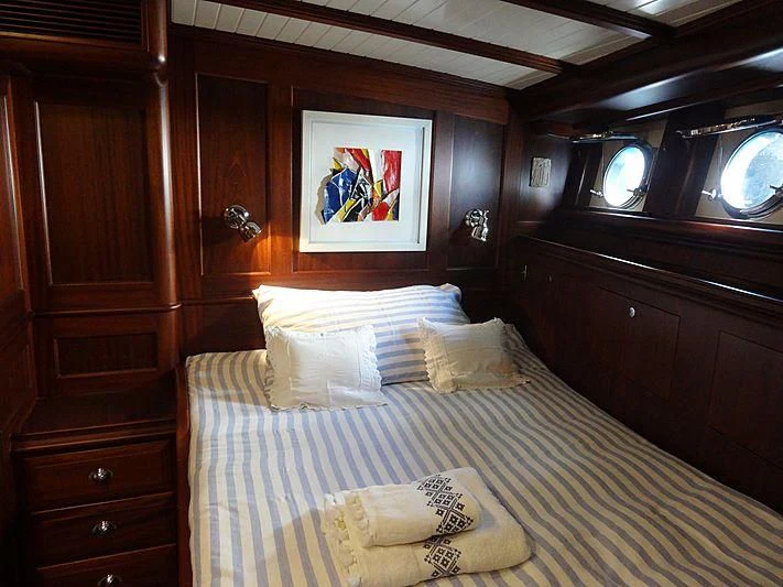 a bed with a white sheet and pillows in a room with wood cabinets aboard ILIOS Yacht for Sale