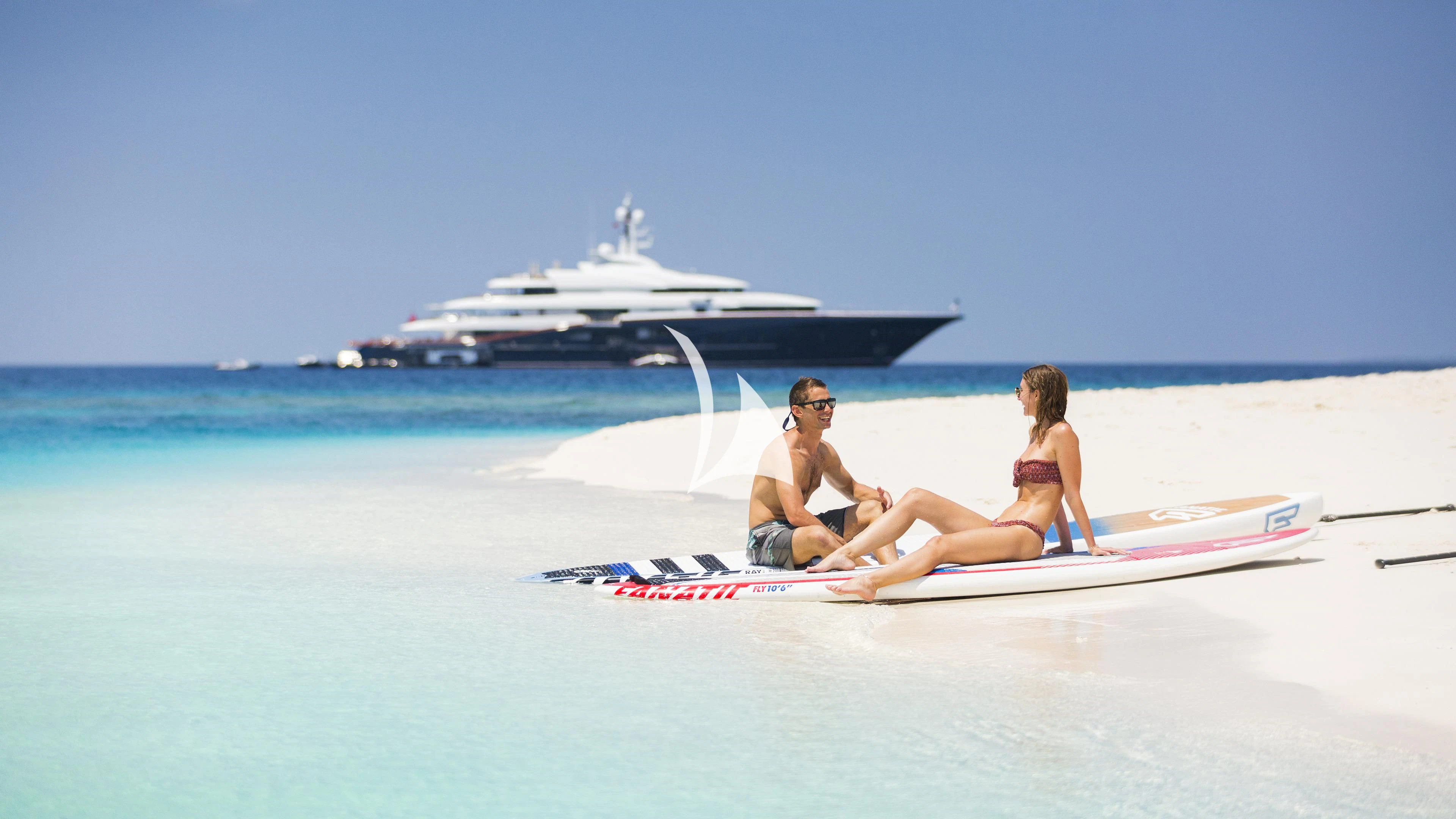 a man and woman sitting on a surfboard on a beach aboard NIRVANA Yacht for Sale