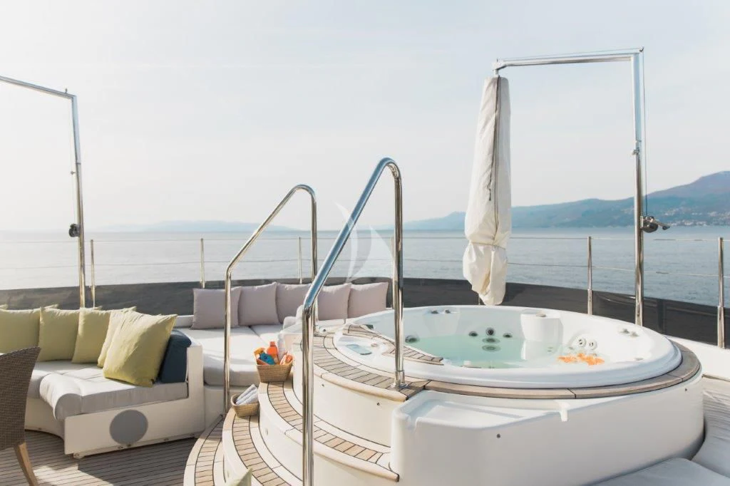 a large white bed with a white pillow and a white chair on a balcony overlooking a body of aboard LADY TRUDY Yacht for Charter