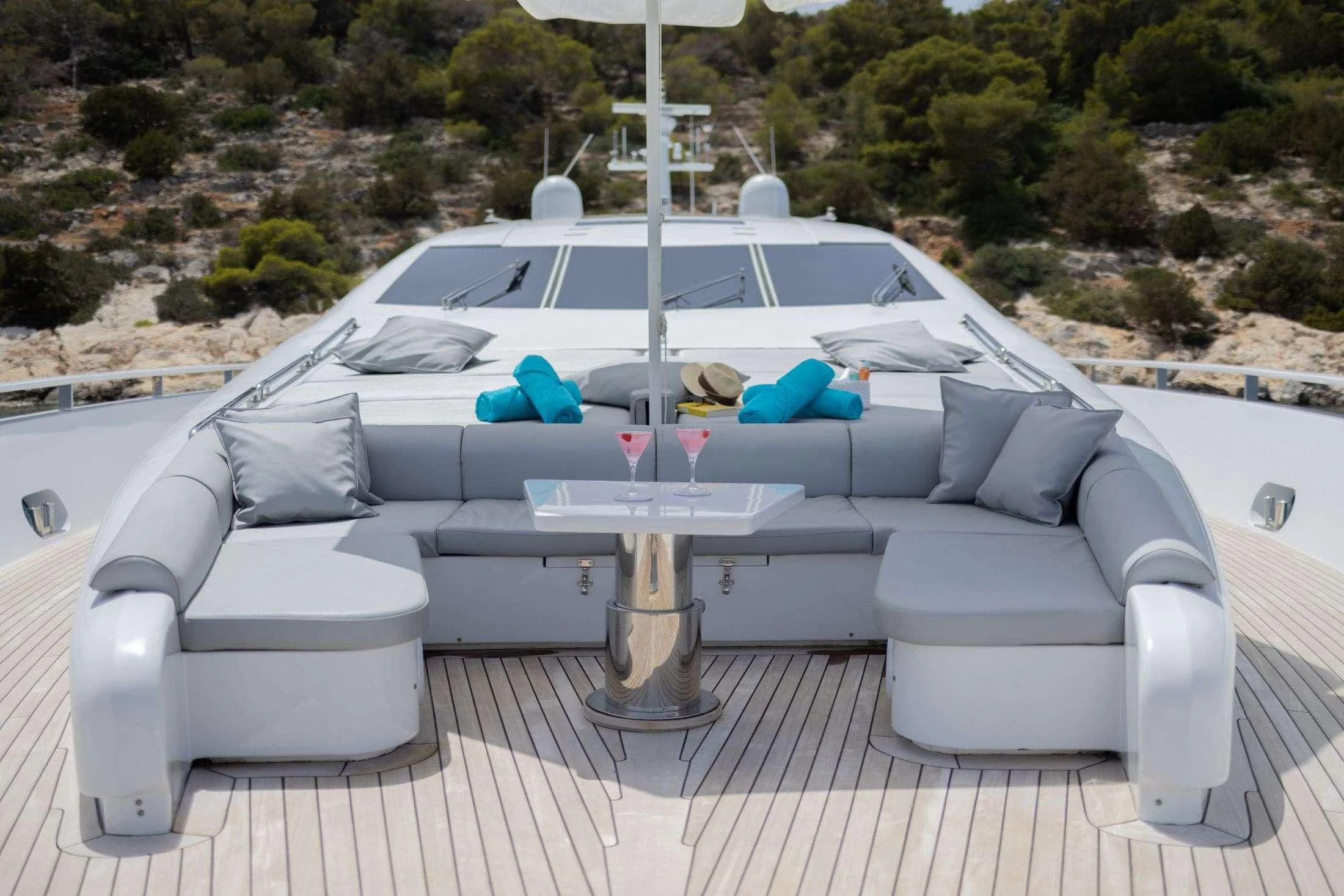 a white lounge chair with a table and a white sofa on a patio with trees and a hill aboard MAC Yacht for Sale