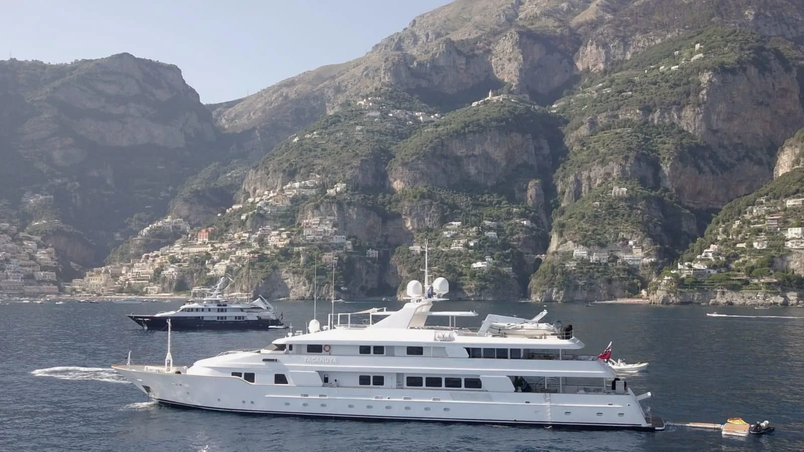 a couple of boats on a body of water by a mountain aboard TACANUYA Yacht for Charter